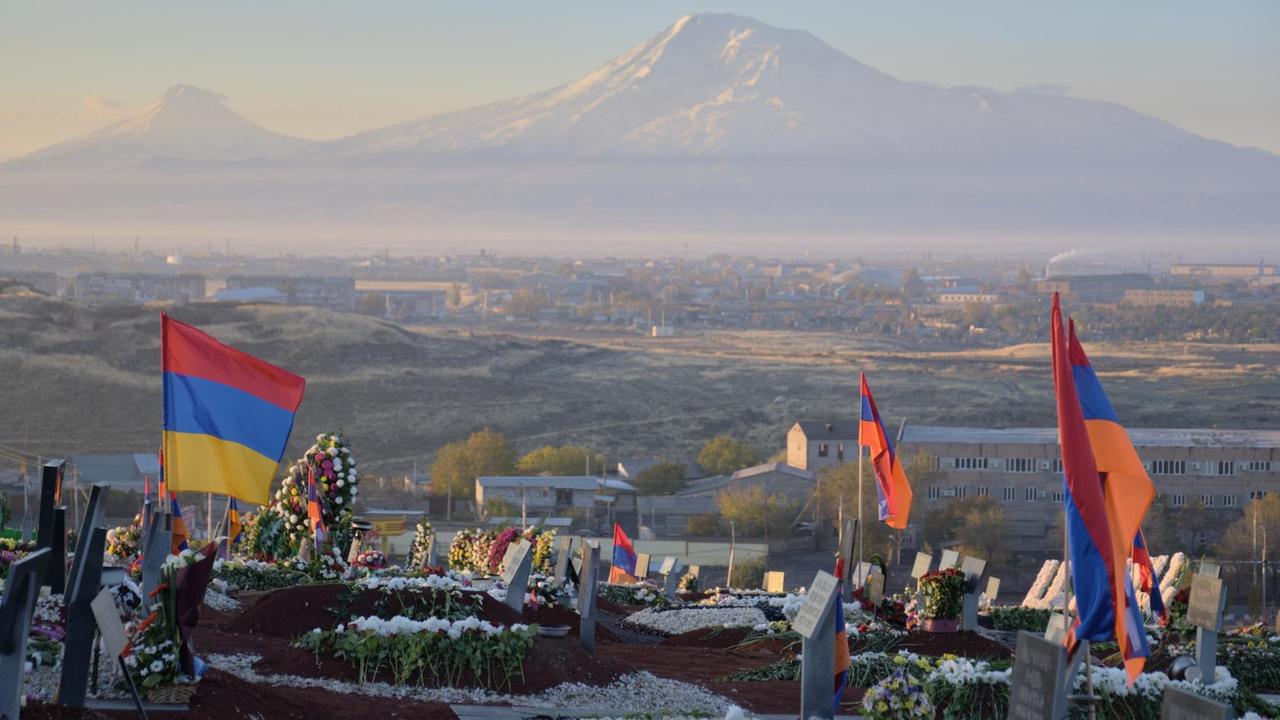 Auf dem Friedhof Jerewan sind Gräber und armenische Flaggen zu sehen. Im Hintergrund ist der Berg Ararat.
