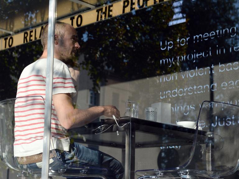 Der niederländische Künstler Dries Verhoeven sitzt am 04.010.2014 bei der Kunstaktion "wanna play ?" in einem Glascontainer auf dem Heinrichplatz in Berlin. Er chattet über die Dating-App Grindr während Passanten die Kommunikation auf einer LED-Wand hinter ihm mitverfolgen können.