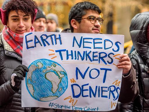 New Yorker demonstrieren gegen Trumps Kabinett, zu dem auch Personen gehören, die bestreiten, dass es einen Klimawandel gibt. Eine Frau hält ein Schild in der Hand, auf dem steht: "Earth needs thinkers not deniers". Die Erde braucht Denker, keine Leugner.