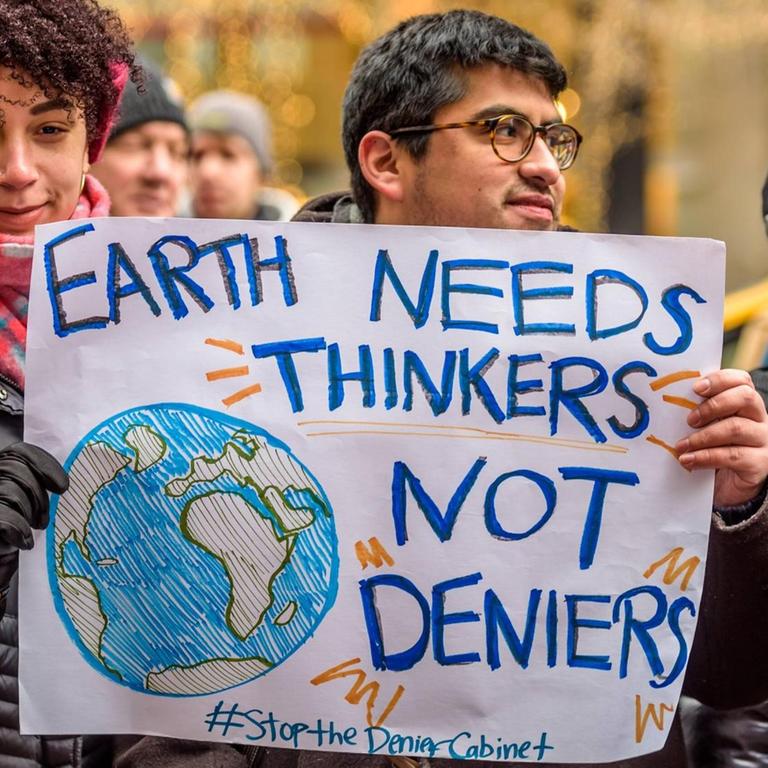 New Yorker demonstrieren gegen Trumps Kabinett, zu dem auch Personen gehören, die bestreiten, dass es einen Klimawandel gibt. Eine Frau hält ein Schild in der Hand, auf dem steht: "Earth needs thinkers not deniers". Die Erde braucht Denker, keine Leugner. 