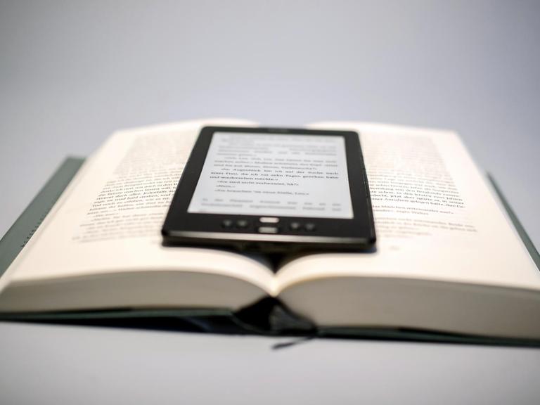 Ein E-Book-Reader liegt auf einem aufgeschlagenen Buch