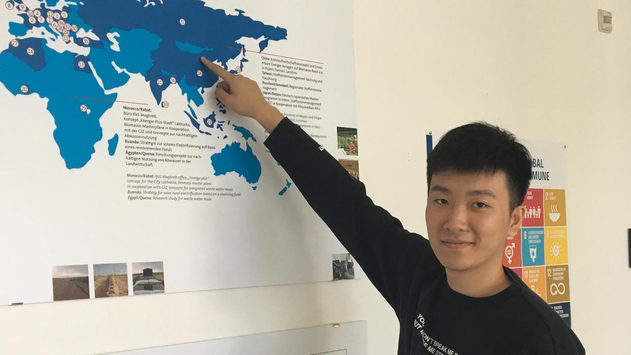 Informatik-Student Eric zeigt stehend auf eine Landkarte, auf der in blau Afrika, Asien und Europa zu sehen ist. Informatik-Student Eric zeigt stehend auf eine Landkarte, auf der in blau Afrika, Asien und Europa zu sehen ist.