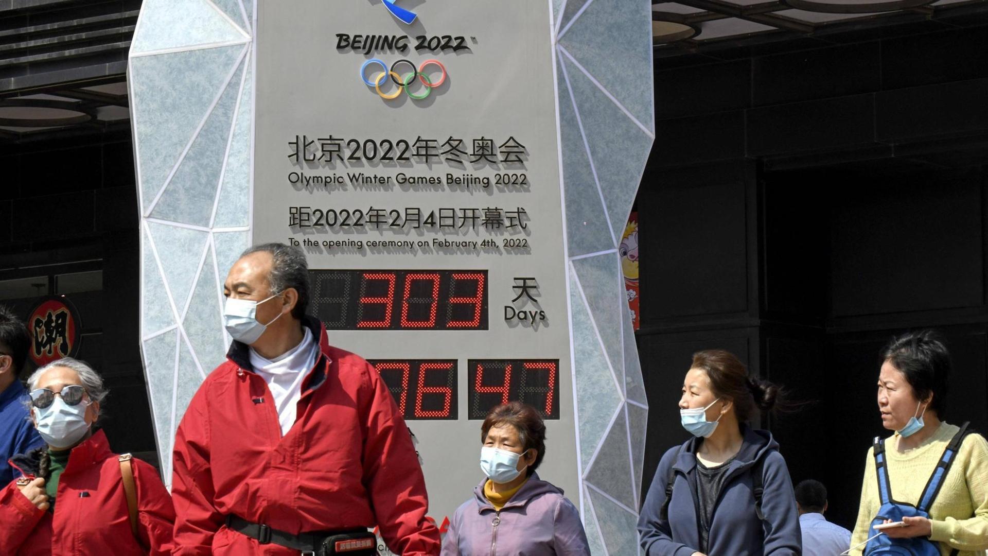 Menschen in Anoraks, mit medizinischen Mund-Nase-Masken zum Schutz vor der Covid19-Pandemie, stehen auf einem Platz in Peking vor einer Uhr mit Digitalanzeige, welche die Zeit bis zum Beginn der olympischen Winterspiele 2022 in Peking herunterzählt. Menschen in Anoraks, mit medizinischen Mund-Nase-Masken zum Schutz vor der Covid19-Pandemie, stehen auf einem Platz in Peking vor einer Uhr mit Digitalanzeige, welche die Zeit bis zum Beginn der olympischen Winterspiele 2022 in Peking herunterzählt.