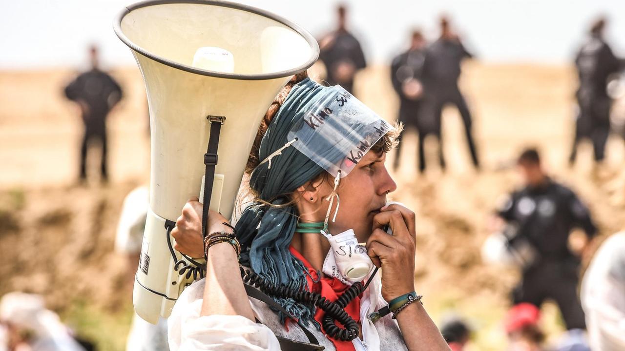 Sprecherin mit Megafon, im Hintergrund Polizisten - Protestaktion von "Ende Gelände" für den sofortigen Kohleausstieg Sprecherin mit Megafon, im Hintergrund Polizisten - Protestaktion von "Ende Gelände" für den sofortigen Kohleausstieg