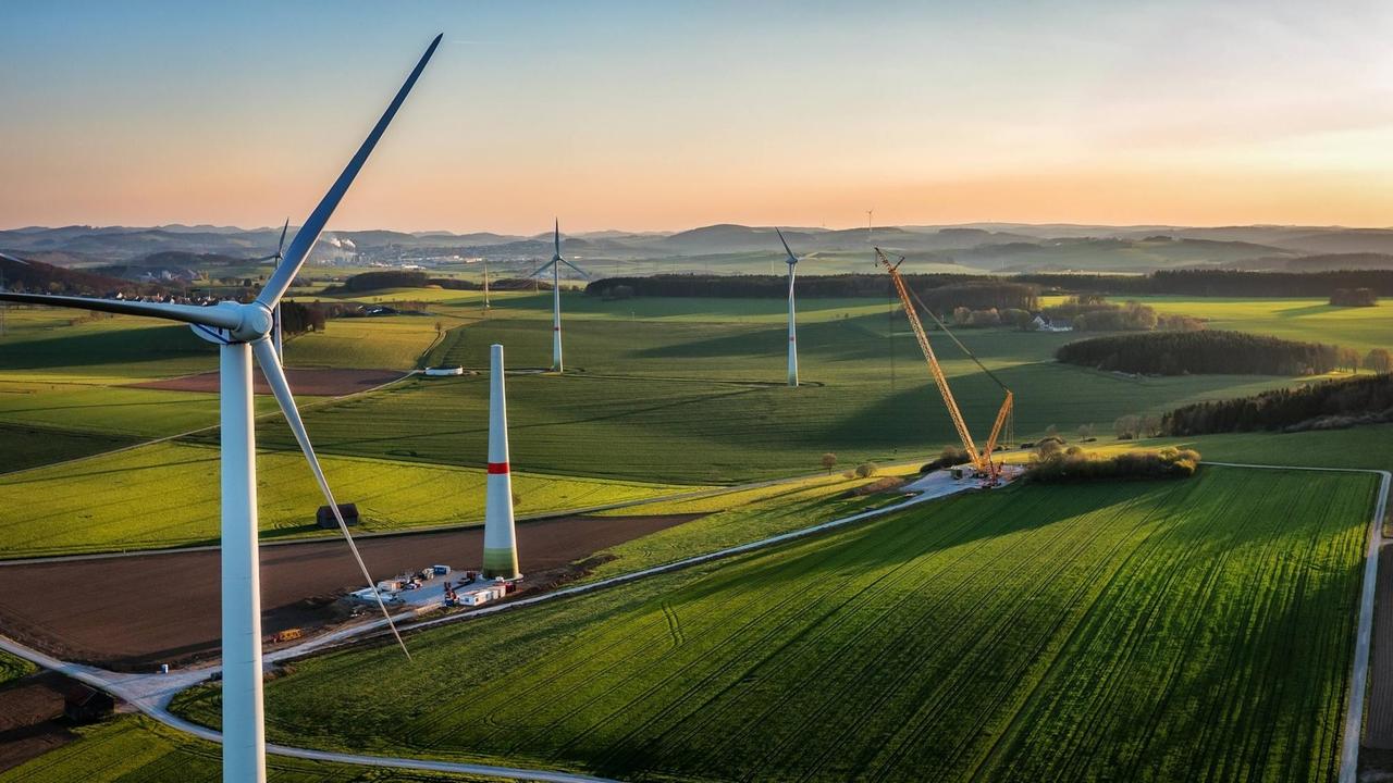 Mehrere Windräder wurden mit einer Drohne von oben aufgenommen und sind im Abendlicht zu sehen. Mehrere Windräder wurden mit einer Drohne von oben aufgenommen und sind im Abendlicht zu sehen.