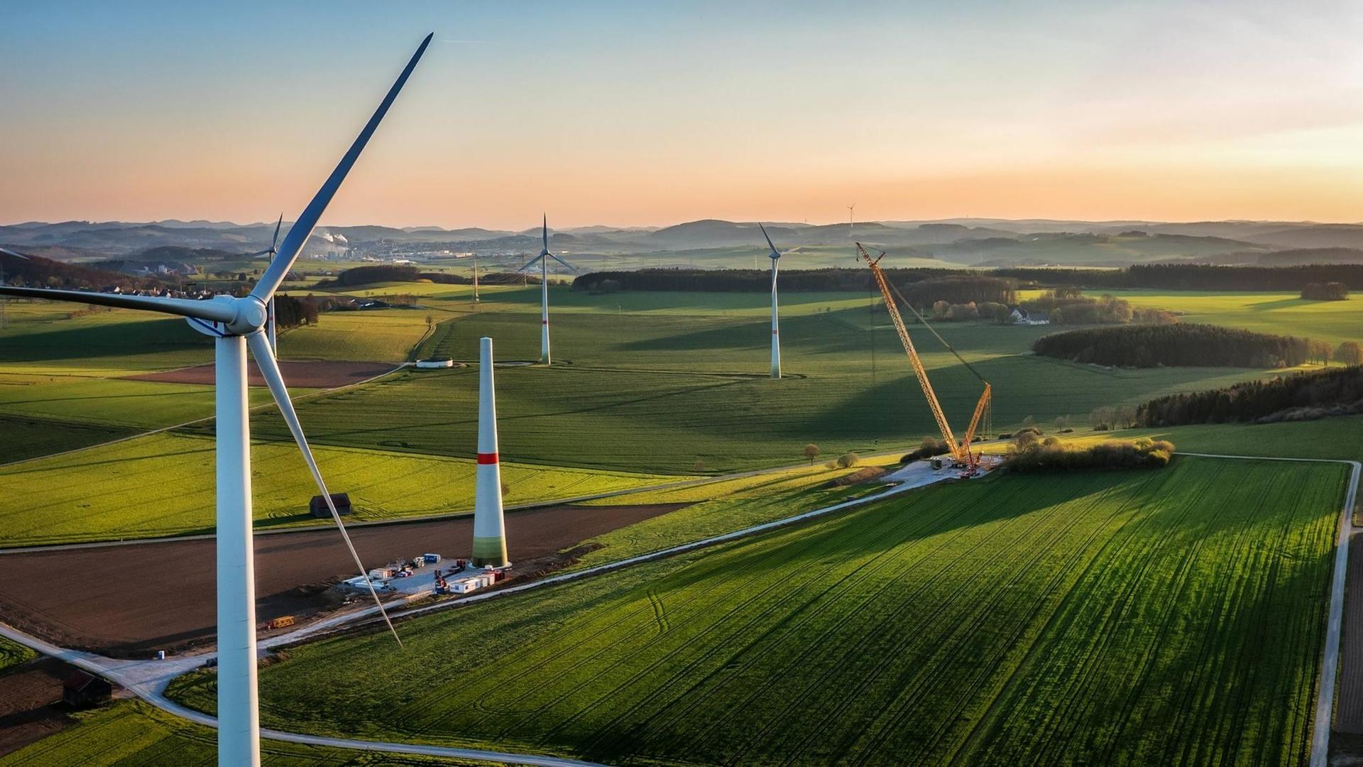 Mehrere Windräder wurden mit einer Drohne von oben aufgenommen und sind im Abendlicht zu sehen. Mehrere Windräder wurden mit einer Drohne von oben aufgenommen und sind im Abendlicht zu sehen.