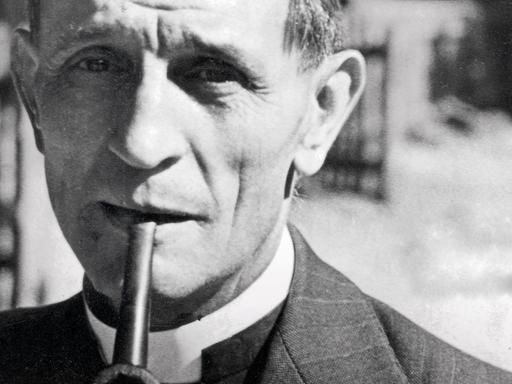 Eine historische Aufnahme von Martin Niemöller, evangelischer Pastor und Theologer, im Anzug und Pfeife im Mund.