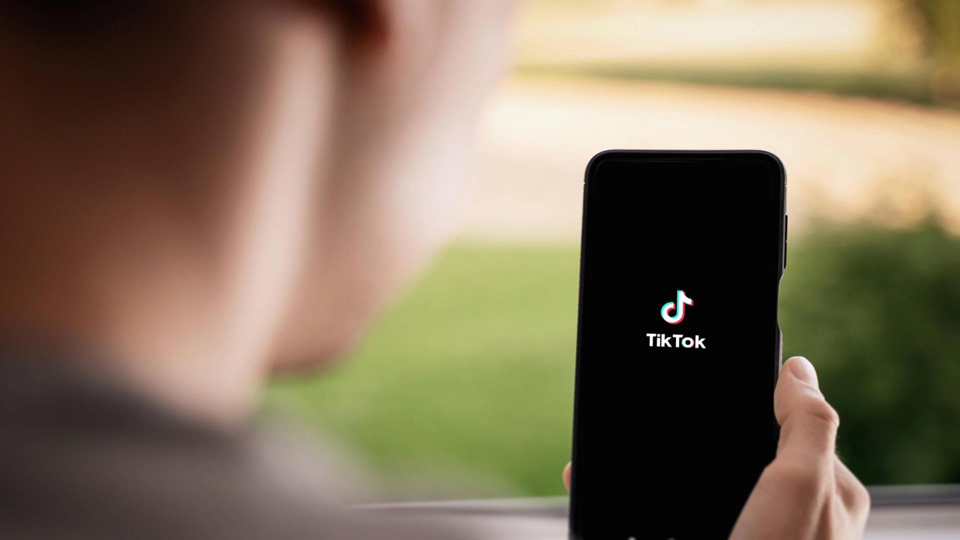 Ein junger Mensch hält ein Smartphone in der Hand, auf dem TikTok-App zu sehen ist. Ein junger Mensch hält ein Smartphone in der Hand, auf dem TikTok-App zu sehen ist.