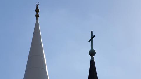 Die Spitze des Minaretts der Yavus Sultan Selim Moschee mit dem Halbmond und das Kreuz auf der Kirchturmspitze der Liebfrauenkirche in Mannheim.