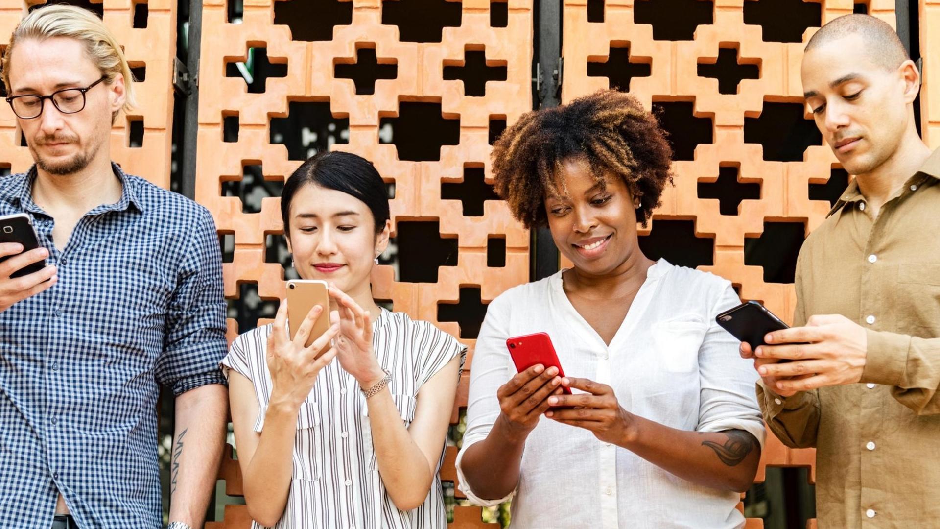 Vier Menschen stehen nebeneinander und jeder verwendet das eigene Smartphone. Vier Menschen stehen nebeneinander und jeder verwendet das eigene Smartphone.
