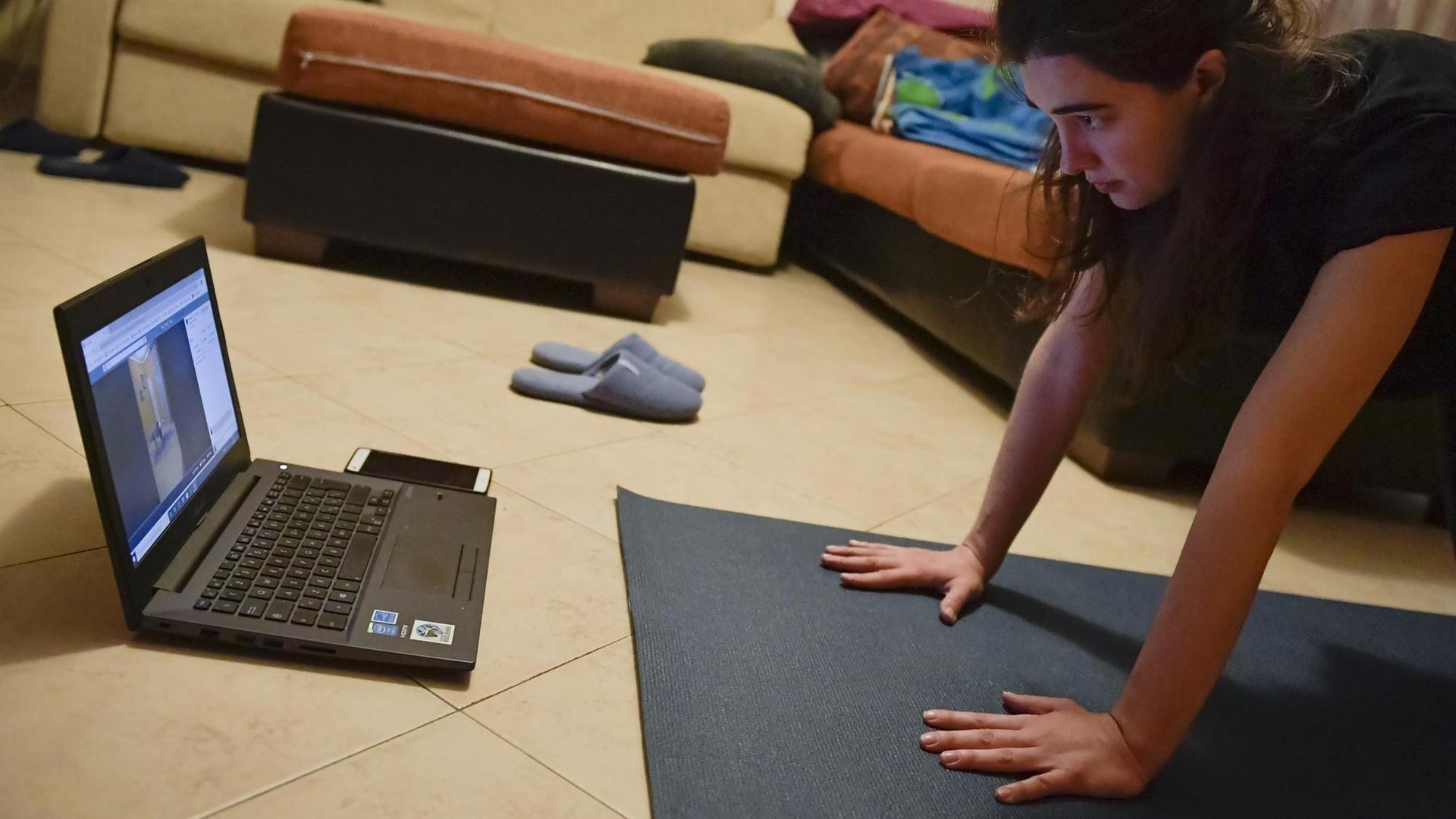 Ein Mädchen folgt einer Online Yoga-Klasse in ihrem Wohnzimmer in Turin, Italien. 14. März 2020. Ein Mädchen folgt einer Online Yoga-Klasse in ihrem Wohnzimmer in Turin, Italien. 14. März 2020.