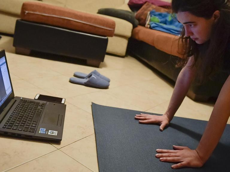 Ein Mädchen folgt einer Online Yoga-Klasse in ihrem Wohnzimmer in Turin, Italien. 14. März 2020.