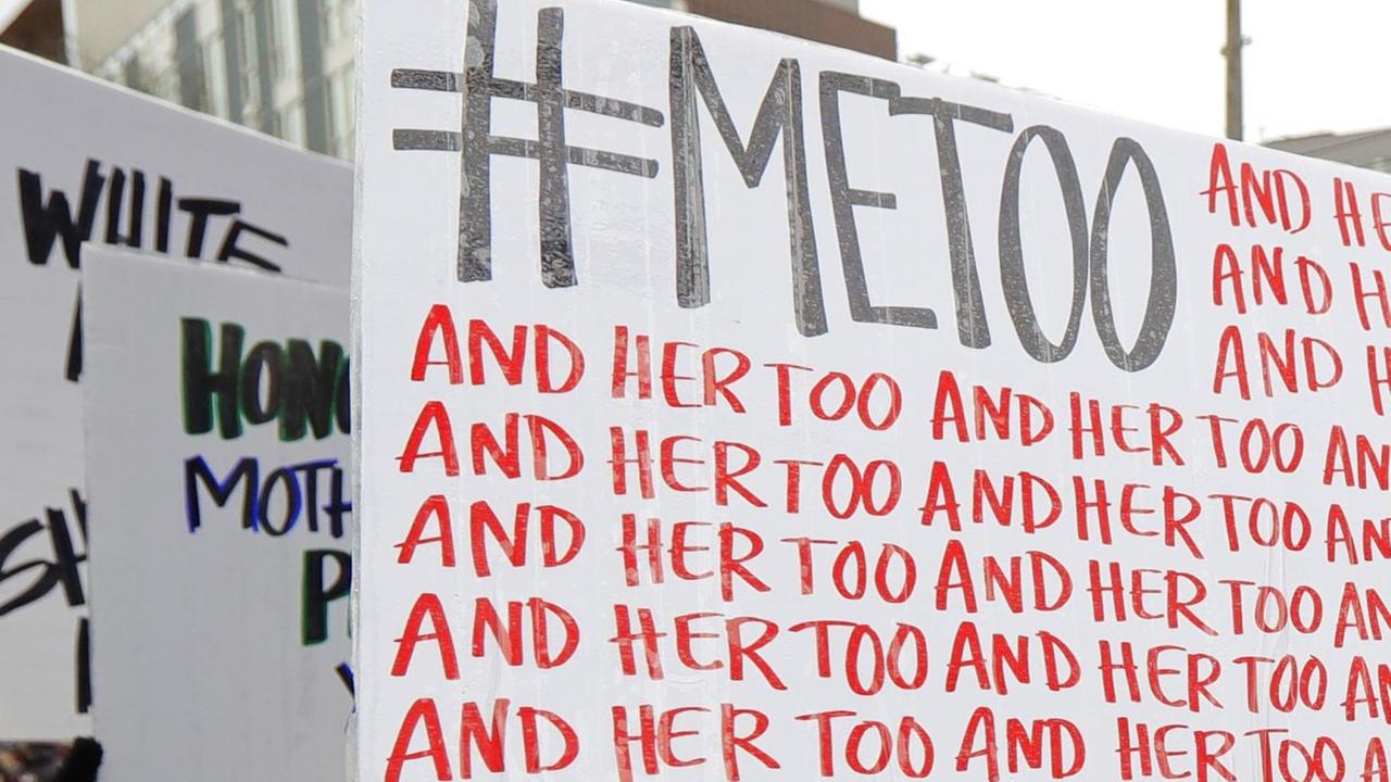 Eine Demonstrantin hält ein Schild mit dem Twitter-Hashtag #MeToo und der sich wiederholenden Aufschrift "and her too" in die Höhe.