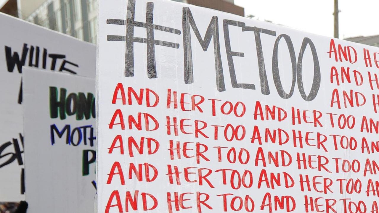 Eine Demonstrantin hält ein Schild mit dem Twitter-Hashtag #MeToo und der sich wiederholenden Aufschrift "and her too" in die Höhe. Eine Demonstrantin hält ein Schild mit dem Twitter-Hashtag #MeToo und der sich wiederholenden Aufschrift "and her too" in die Höhe.