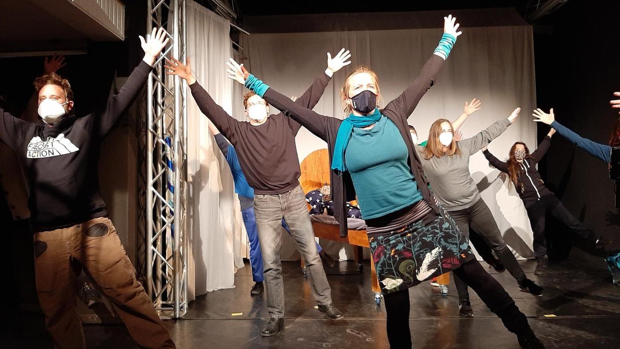 Mehrere Schauspieler stehen mit ausgestreckten Armen und Beinen auf der Bühne. Alle tragen Masken. Mehrere Schauspieler stehen mit ausgestreckten Armen und Beinen auf der Bühne. Alle tragen Masken.