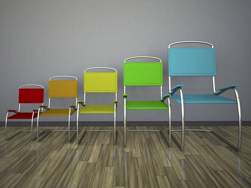 Fünf Stühle in verschiedenen Farben und Größen stehen nebeneinander. Von links nach rechts werden die Stühle immer größer.