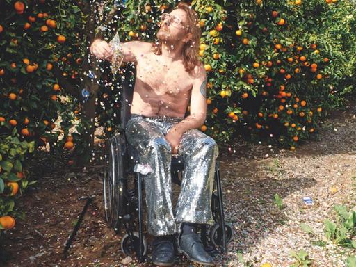 Der Fotograf Daniel Josefsohn im Rollstuhl - freier Oberkörper, silberne Hose, die Augen geschlossen - bewirft sich mit Konfetti