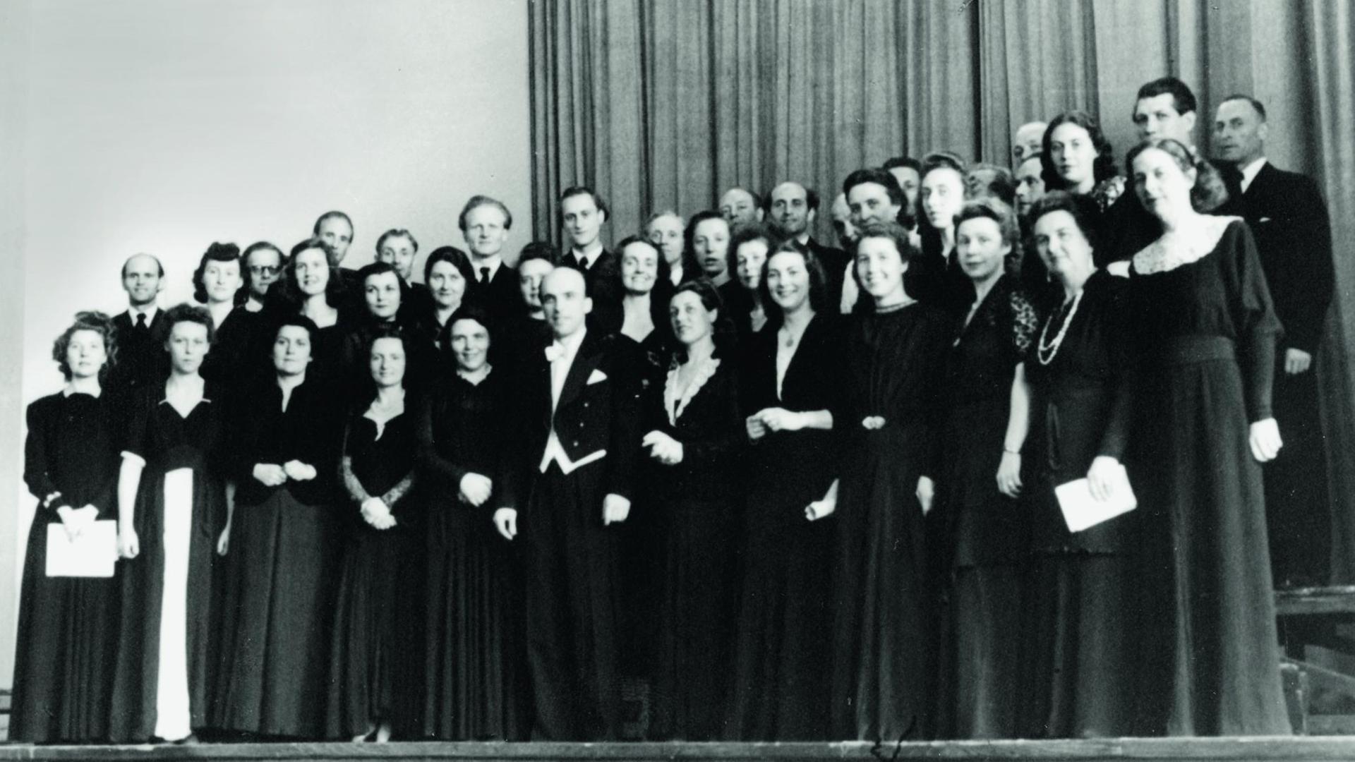 Der RIAS Kammerchor auf einem schwarz-weiß-Foto in schwarzer Konzertkleidung, in der Mitte der Dirigent Herbert Froitzheim (im Frack) Aufnahme von 1949 Der RIAS Kammerchor auf einem schwarz-weiß-Foto in schwarzer Konzertkleidung, in der Mitte der Dirigent Herbert Froitzheim (im Frack) Aufnahme von 1949
