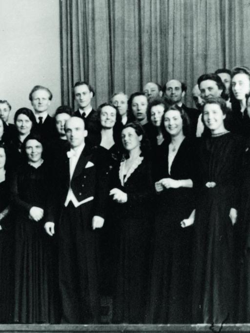 Der RIAS Kammerchor auf einem schwarz-weiß-Foto in schwarzer Konzertkleidung, in der Mitte der Dirigent Herbert Froitzheim (im Frack) Aufnahme von 1949