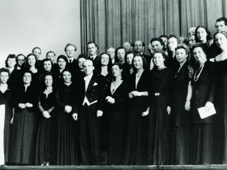 Der RIAS Kammerchor auf einem schwarz-weiß-Foto in schwarzer Konzertkleidung, in der Mitte der Dirigent Herbert Froitzheim (im Frack) Aufnahme von 1949