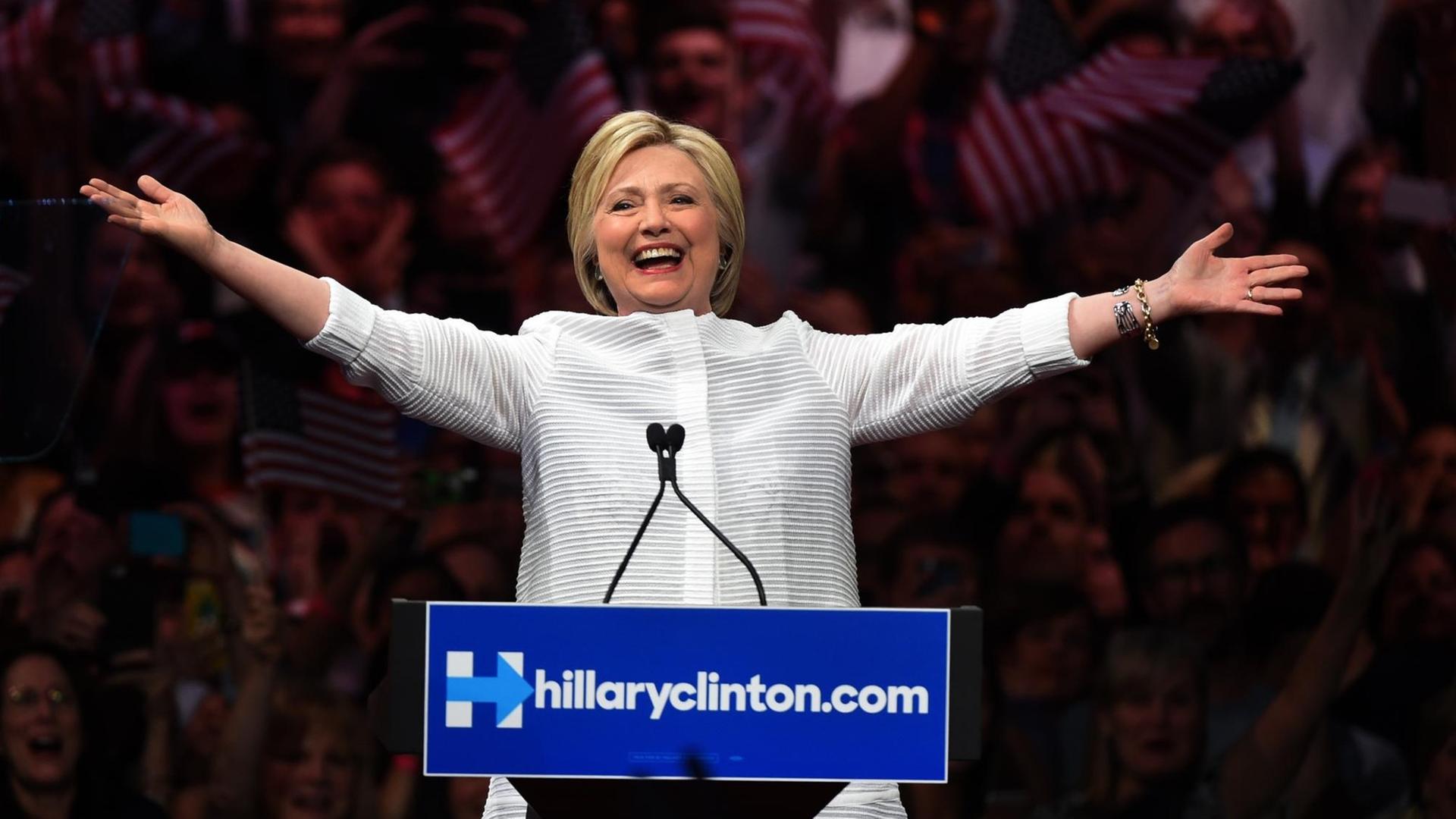Hillary Clinton steht vor jubelnden Anhängern und breitet lächelnd die Arme aus. Hillary Clinton steht vor jubelnden Anhängern und breitet lächelnd die Arme aus.