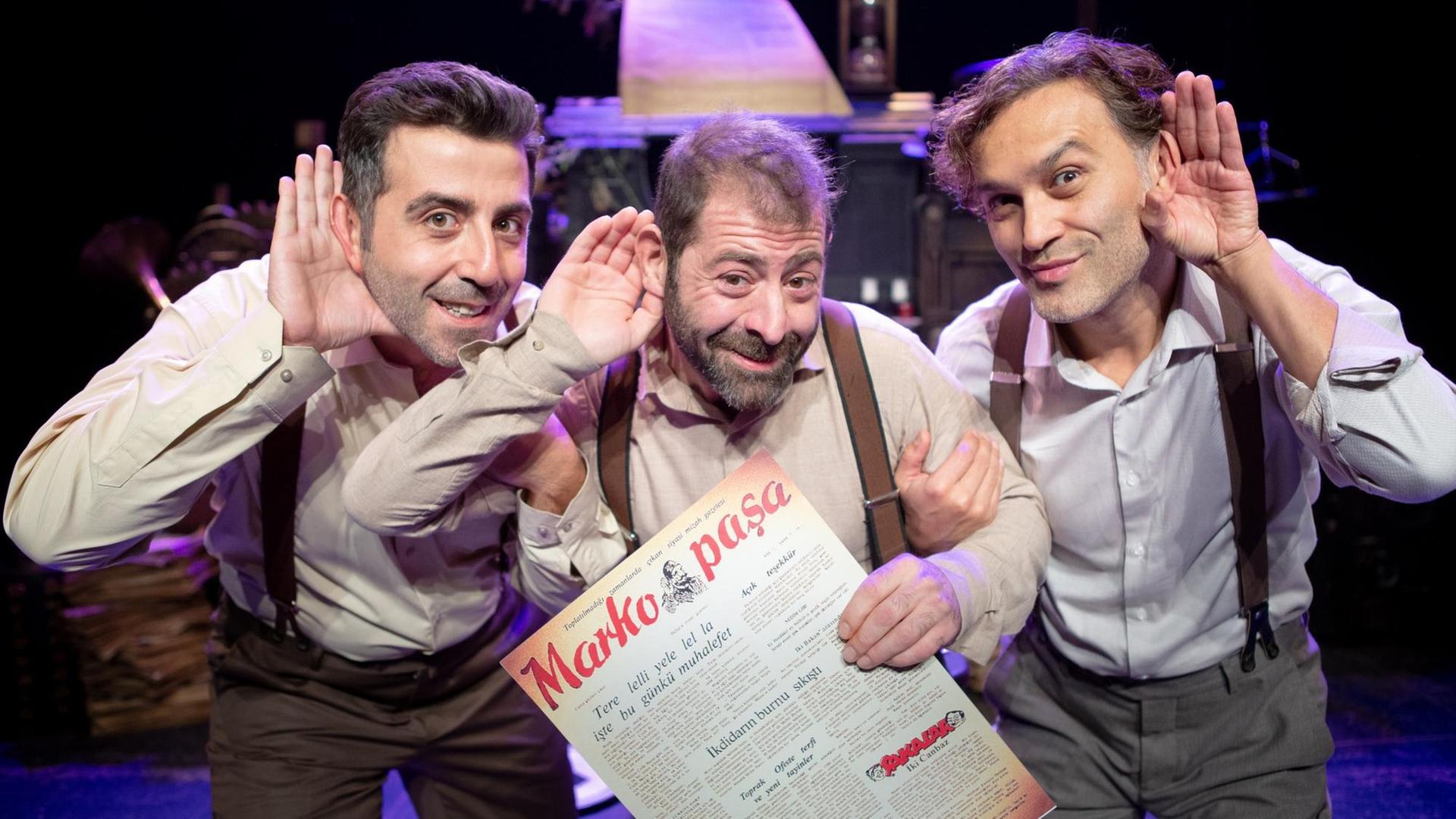 Fatih Koyunoğlu, Erdem Akakçe, Bülent Çolak vom Theater Tiyatroadam gucken in die Kamera und halten jeweils eine Hand hinter die Ohren, als ob sie etwas Bestimmtes hören wollen. Fatih Koyunoğlu, Erdem Akakçe, Bülent Çolak vom Theater Tiyatroadam gucken in die Kamera und halten jeweils eine Hand hinter die Ohren, als ob sie etwas Bestimmtes hören wollen.