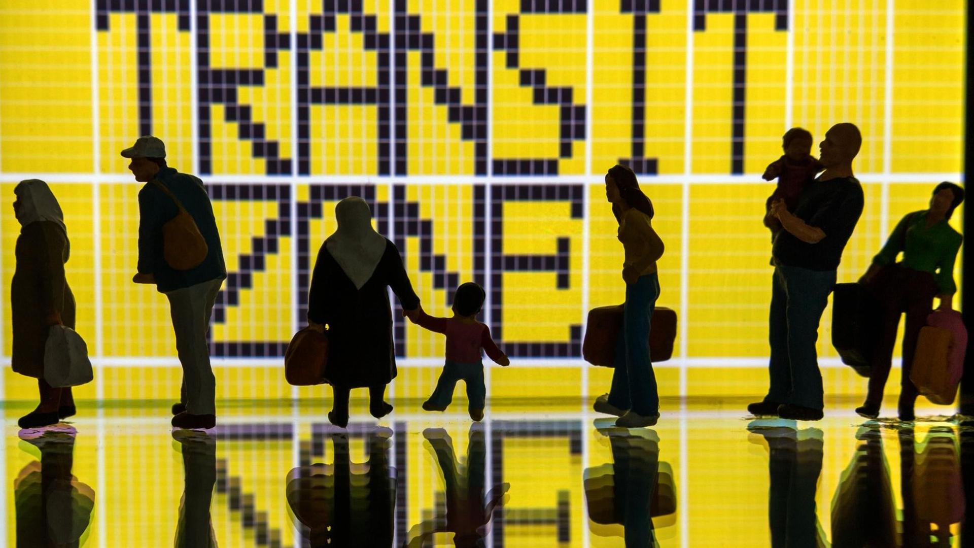 Modellfiguren stehen vor einem Display mit dem Schriftzug "Transitzone" (gestelltes Foto). Modellfiguren stehen vor einem Display mit dem Schriftzug "Transitzone" (gestelltes Foto).