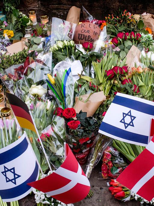 Vor der jüdischen Synagoge in Kopenhagen liegen nach dem Anschlag tausende Blumen; einige Menschen haben auch kleine Fahnen von Israel, Dänemark und Deutschland in das Blumenmeer gesteckt.