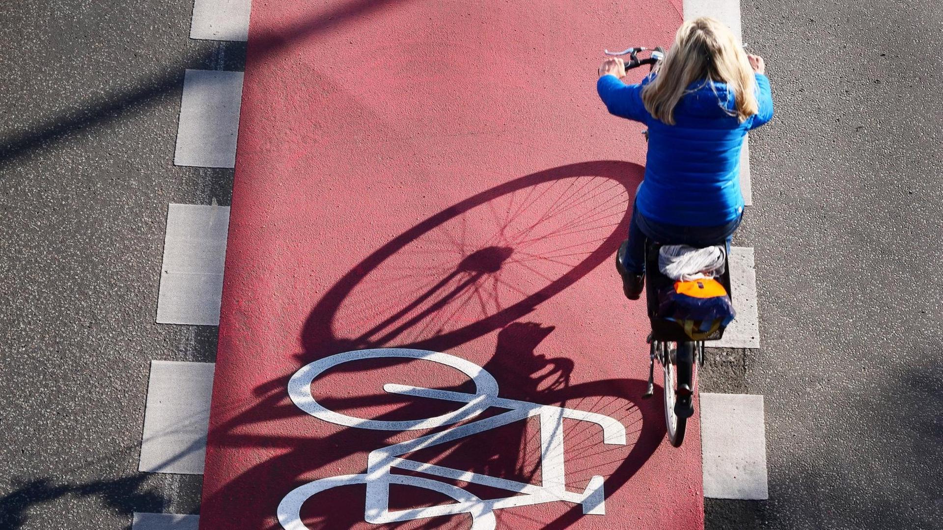 Ein Fahrrad ist auf einem neuen, roten Radweg auf der Schlossstrasse in Steglitz aufgemalt. Eine Frau faehrt mit ihrem Rad auf dem Radweg. Ein Fahrrad ist auf einem neuen, roten Radweg auf der Schlossstrasse in Steglitz aufgemalt. Eine Frau faehrt mit ihrem Rad auf dem Radweg.
