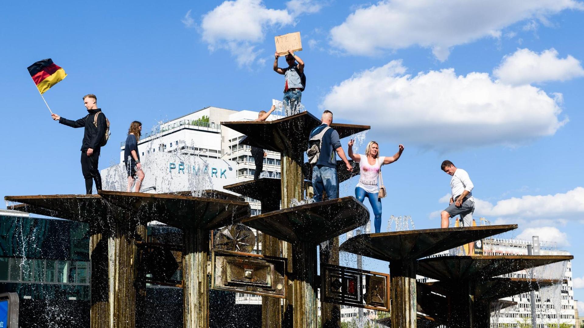 Demonstration gegen die Corona-Verordnungen am Berliner Alexanderplatz. Menschen stehen in einem Springbrunnen. Ein Mann hält die deutsche Flagge in der Hand. Demonstration gegen die Corona-Verordnungen am Berliner Alexanderplatz. Menschen stehen in einem Springbrunnen. Ein Mann hält die deutsche Flagge in der Hand.