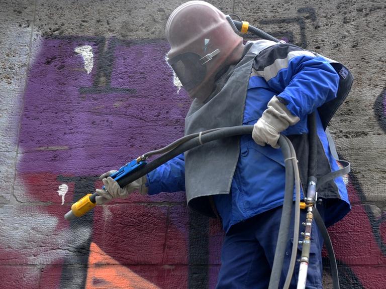 Ein Arbeiter des Baureferats mit Schutzhelm entfernt von der Ludwigsbrücke in München ein Graffiti.