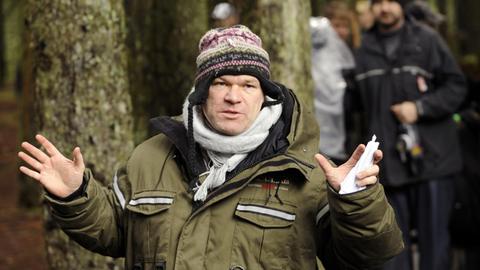 Regisseur Uwe Boll hat eine Strickmütze auf und zeigt die Handflächen.
