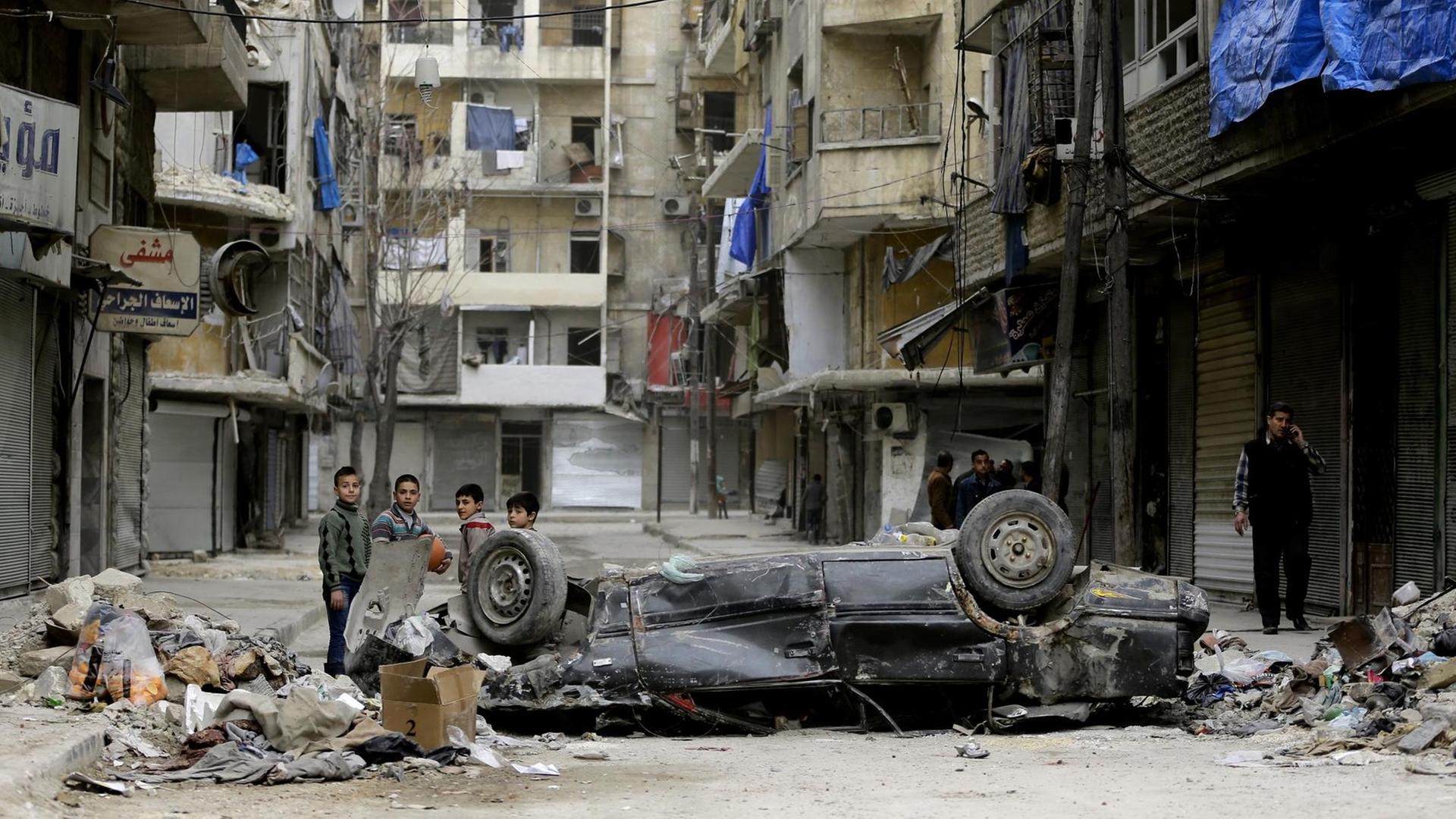 Kinder spielen in einem ehemals von Rebellen gehaltenen Stadtteil von Aleppo zwischen zerstörten Häusern und hinter einem Auto, das auf dem Dach liegt.