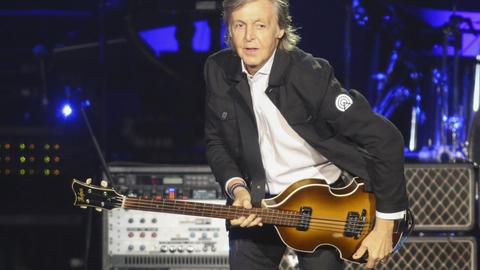 Paul McCartney mit einem Bass posierend auf der Bühne