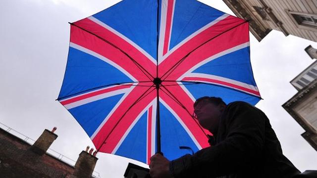Ein Mann mit einem Regenschirm in den Farben der britischen Fahne vor dem St James's Palace in London am 23.10.2013. An diesem Tag wird Prinz George, der Sohn von Prinz William und seiner Frau Catherine getauft.