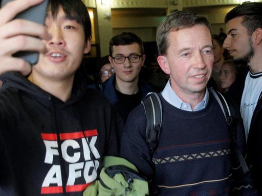 Bernd Lucke drängt sich nach seiner verhinderten Vorlesung aus dem Saal. Neben ihm ein Demonstrant in einem Pullover mit der Aufschrift "FCK AFD".