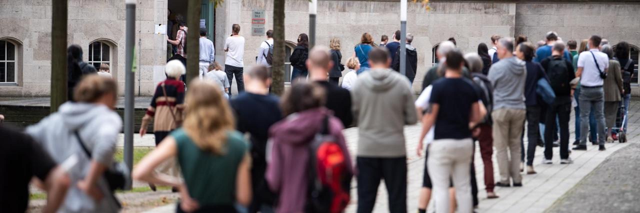 Menschen stehen in einer langen Warte-Schlange auf dem Fuß-Weg Menschen stehen in einer langen Warte-Schlange auf dem Fuß-Weg