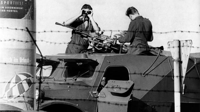 Ein Volkspolizist beobachtet mit einem Fernglas an der kriegsmäßig abgeriegelten Sektorengrenze in der Berliner Friedrichstraße auf einem gepanzerten Fahrzeug mit Maschinengewehr bestückt den Westen. Aufnahme vom September 1961.