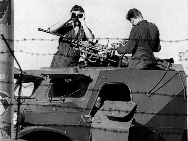 Ein Volkspolizist beobachtet mit einem Fernglas an der kriegsmäßig abgeriegelten Sektorengrenze in der Berliner Friedrichstraße auf einem gepanzerten Fahrzeug mit Maschinengewehr bestückt den Westen. Aufnahme vom September 1961.