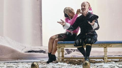 Die Schauspieler Safira Robens und Martin Wuttke sitzen in der Inszenierung des Stücks "Schwarzwasser" von Elfriede Jelinek am Wiener Burgtheater auf einer mit blauem Samt bezogenen Bank.