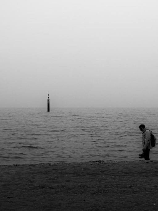 Ein Mann im Schattenriss steht am Meer,
