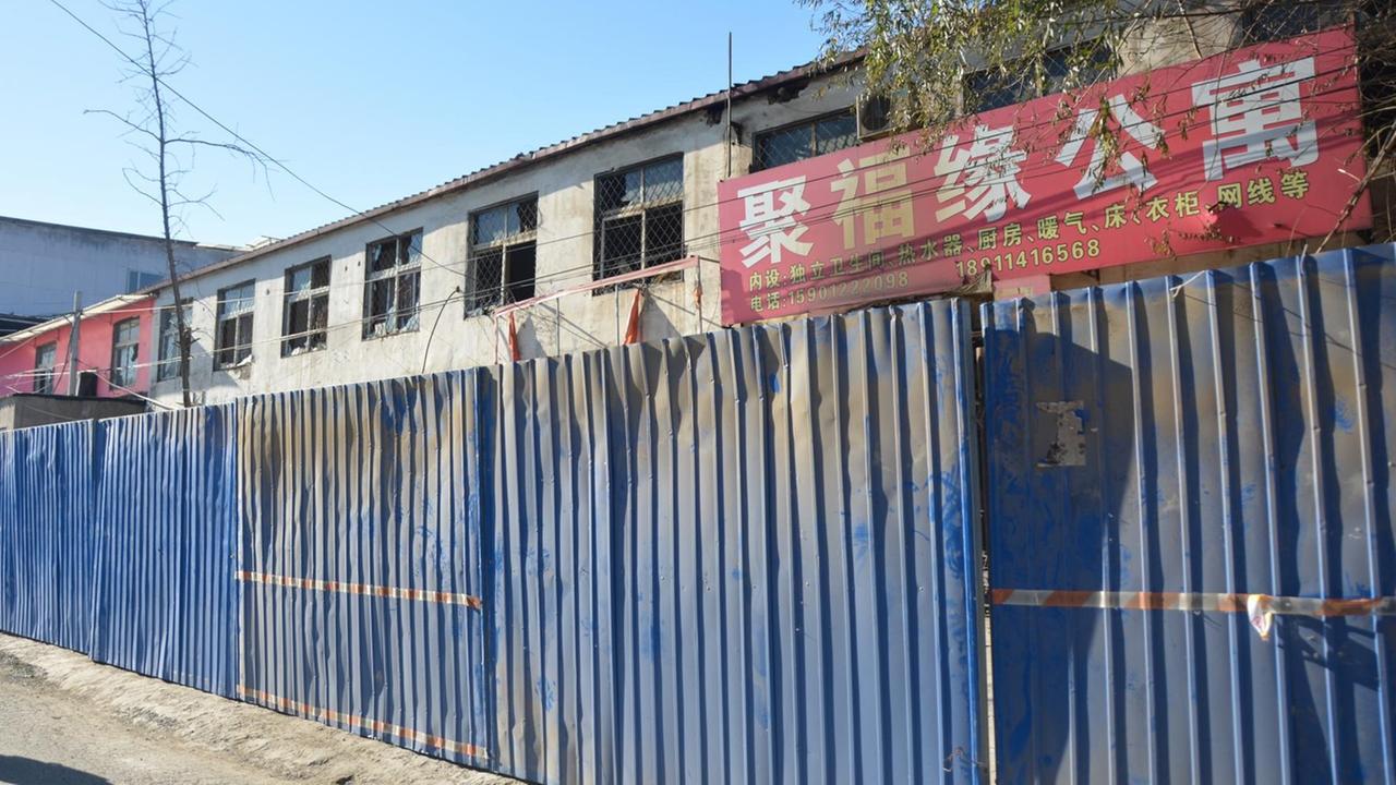 Ein ausgebranntes Appartementhaus in Peking wird von einem blauen Bauzaun gesichert.
