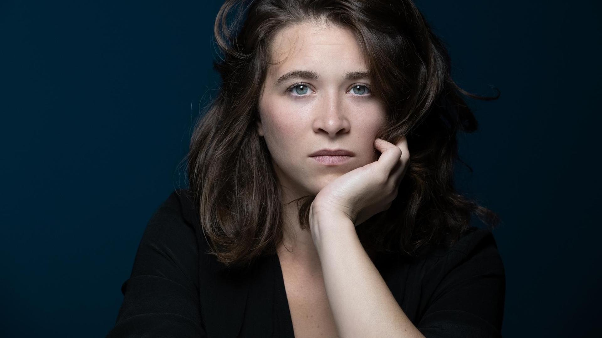 Emma Becker schaut, ihren Kopf auf die Hand gestützt, in die Kamera Emma Becker schaut, ihren Kopf auf die Hand gestützt, in die Kamera