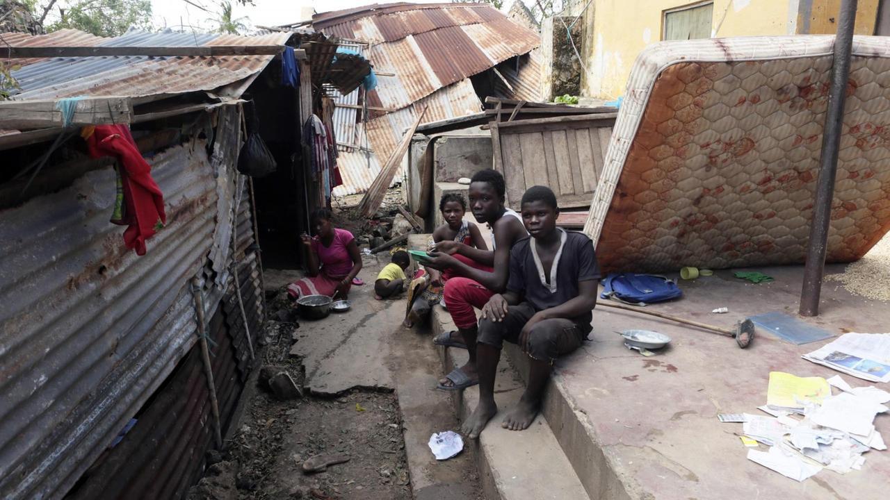 Eine Familie sitzt auf den Stufen zu ihrem stark beschädigten Haus. Eine Familie sitzt auf den Stufen zu ihrem stark beschädigten Haus.