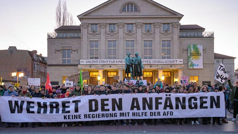 "Wehret den Anfängen - Keine Regierung mit Hilfe der AFD" steht auf einem Transparent, das Demonstranten vor dem Theater und dem Goethe- und Schillerdenkmal halten. Die Menschen demonstrieren gegen den neuen Ministerpräsidenten von Thüringen. "Wehret den Anfängen - Keine Regierung mit Hilfe der AFD" steht auf einem Transparent, das Demonstranten vor dem Theater und dem Goethe- und Schillerdenkmal halten. Die Menschen demonstrieren gegen den neuen Ministerpräsidenten von Thüringen.