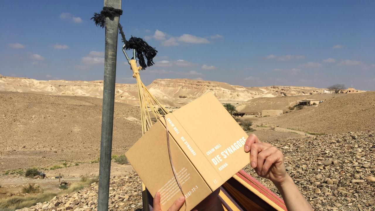 Jemand liest Chaim Nolls "Die Synagoge" in einer Hängematte in der Wüste