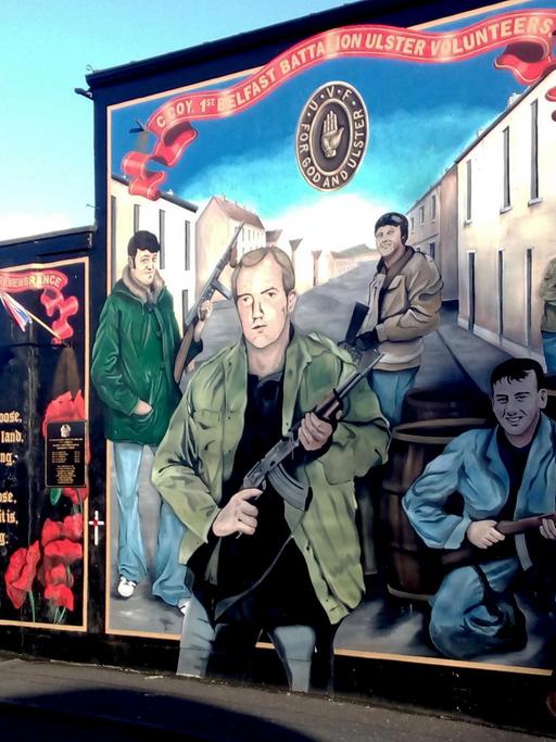 Eine Hauswand mit einer Malerei, auf der Männern mit Gewehren abbildet sind.