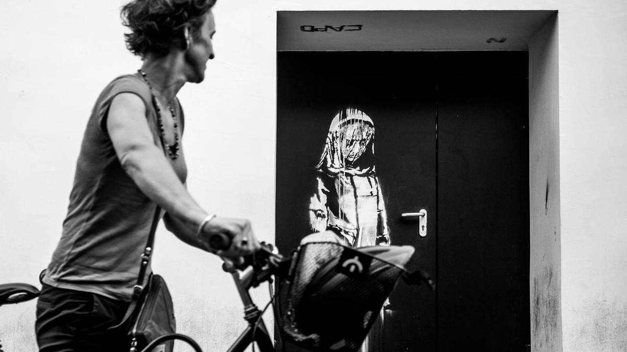 Eine Frau mit einem Fahrrad läuft an einer Installation von Banksy am Pariser Club Bataclan vorbei.