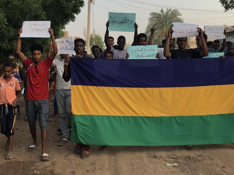 Demonstrierende im Sudan halten Schilder hoch