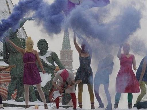 Ein halbes Dutzend maskierte Tänzer und Musiker am Roten Platz, Rauchschwaden steigen auf